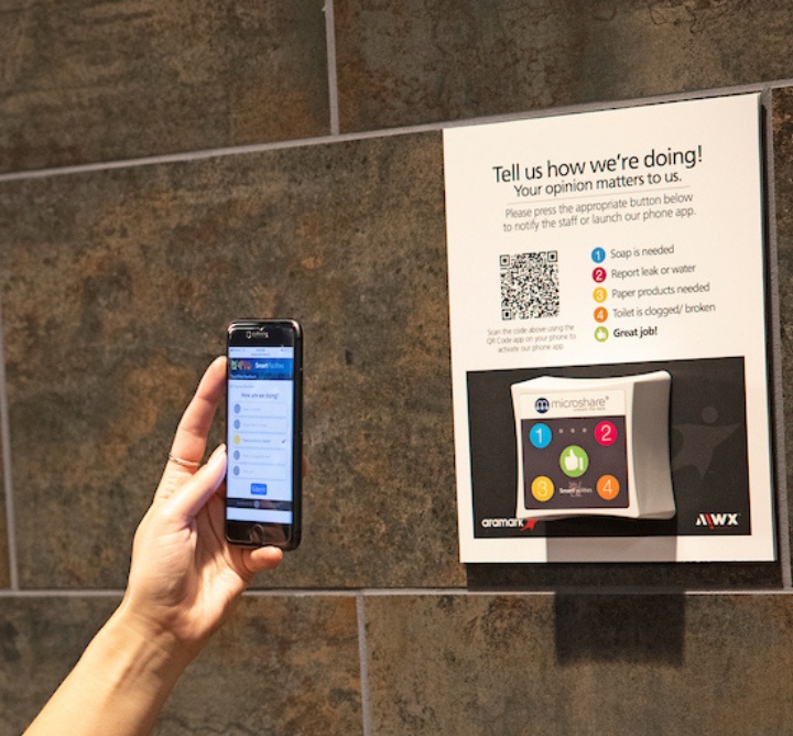 A hand holding up a phone to scan a QR code on the wall for collecting real-time feedback.